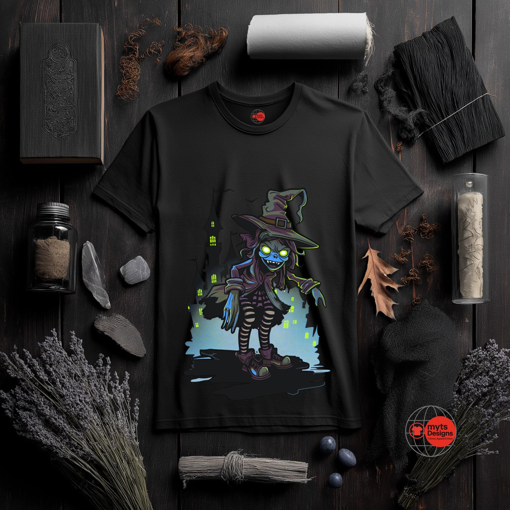 Black t-shirt with a colorful graphic of a witch on a dark wooden surface with Halloween-themed decorations.