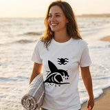 Woman on a beach wearing a white t-shirt with a black graphic design, holding a towel.