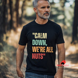 A senior man walking in the woods wearing a black retro-style casual tee featuring bold distressed vintage typography reading “Relax — We’re All Weird Here,” printed on ultra-soft Gildan 64000 cotton.

