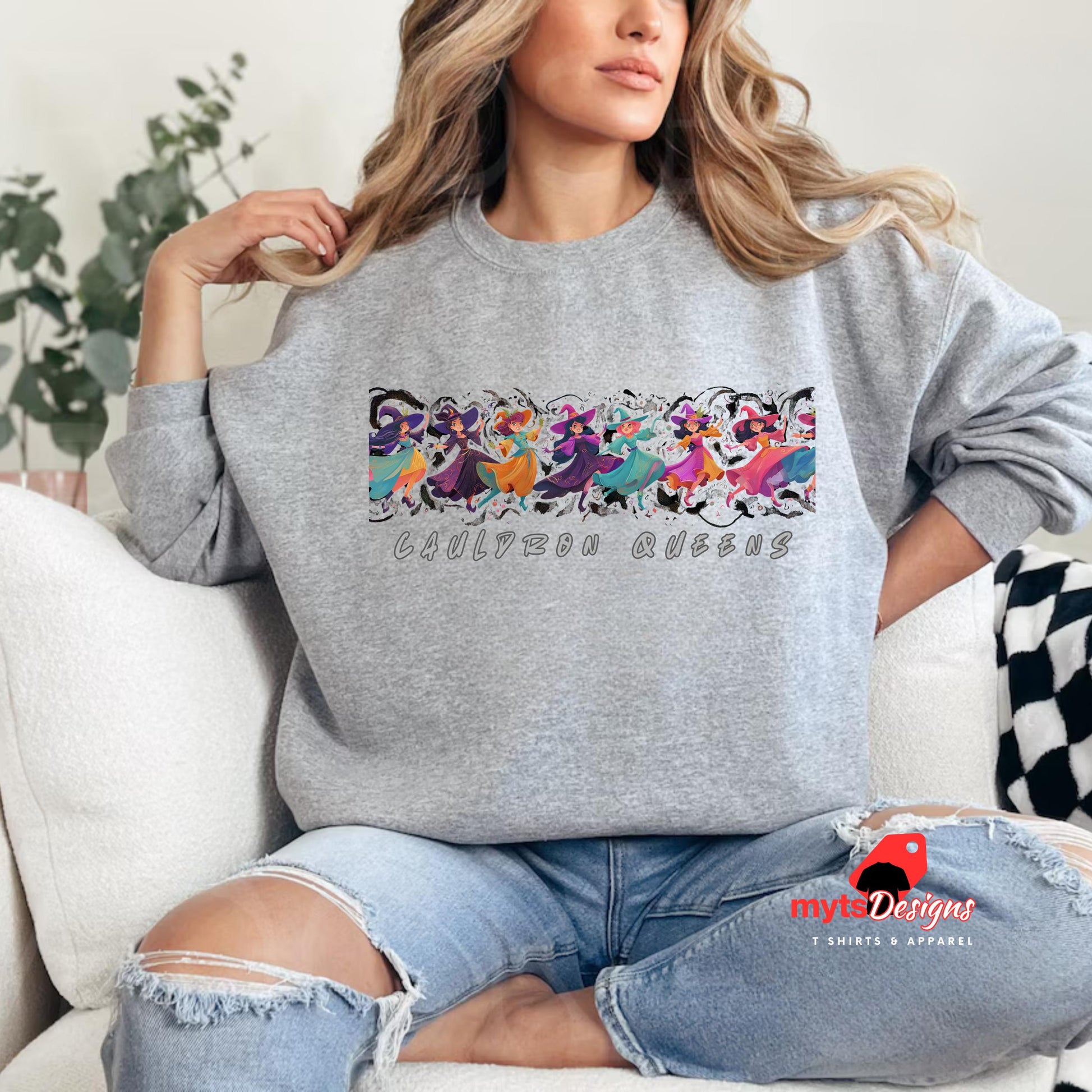 Person wearing a gray sweatshirt with colorful cat designs and text, sitting on a couch.