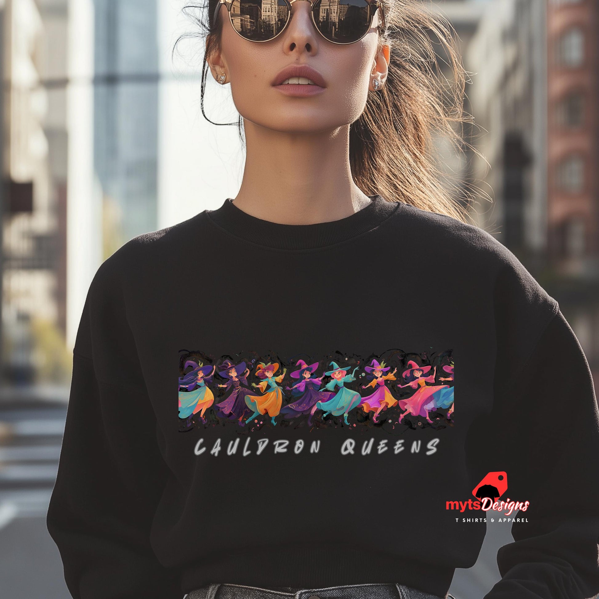 Person wearing a black sweatshirt with 'Cauldron Queens' design and sunglasses, standing in an urban setting.