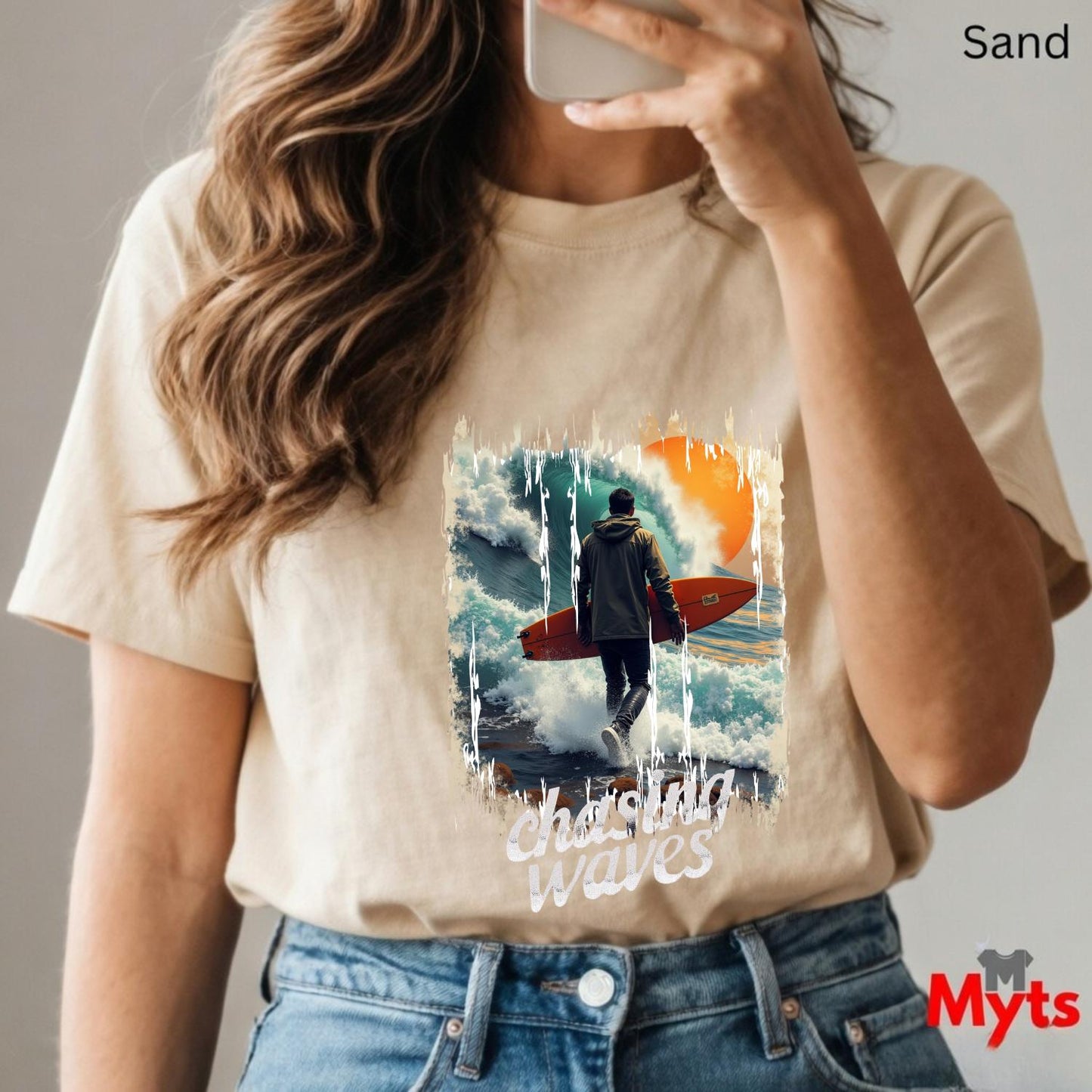 Person wearing a sand t-shirt with a graphic design and text, taking a mirror selfie.