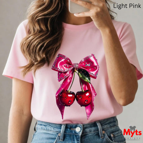 Person wearing a pink t-shirt with a decorative bow and cherries design, holding a phone.