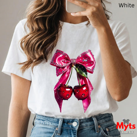 Person wearing a white t-shirt with a pink bow and cherry design, holding a phone.