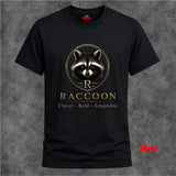 A black short-sleeve crewneck t-shirt featuring a gold and white raccoon graphic with the word 'RACCOON' and the phrase 'Clever - Bold - Adaptable' printed on the front, displayed against a textured gray background.