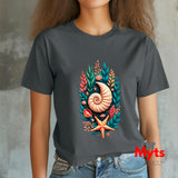 A woman wearing a dark gray t-shirt with a colorful graphic of a nautilus shell, starfish, and seashells. The background is a textured gray wall.