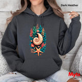 A woman wearing a dark heather charcoal hoodie with a colorful seashell and coral graphic on the front, sitting against a light wood wall. Text overlays read 'Dark Heather' and 'Myts'.