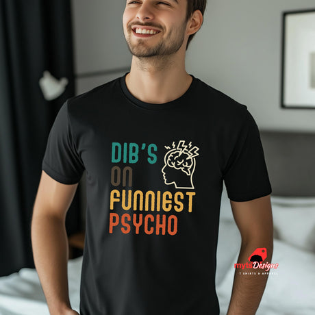 Front view of a man wearing a casual tee featuring retro script that reads “Dibs on Funniest Psycho” in distressed vintage style, printed on ultra-soft black Gildan 64000 cotton
