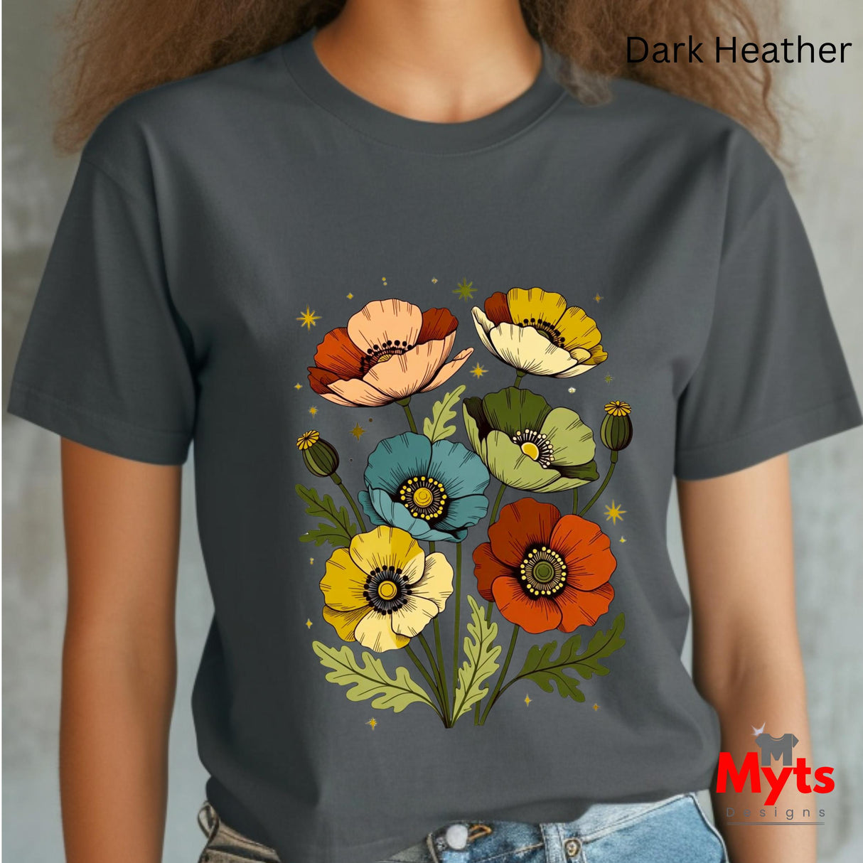 A person wearing a dark heather charcoal gray t-shirt with a colorful graphic of stylized poppy flowers in orange, yellow, blue, and cream. The text 'Dark Heather' is visible in the top right corner, and a 'Myts Designs' logo is in the bottom right corner.