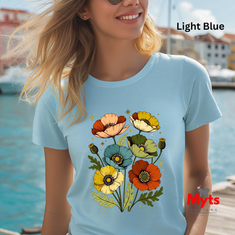 A woman wearing a light blue t-shirt with a colorful poppy floral graphic, set against a sunny outdoor waterfront background. The text 'Light Blue' is visible in the top right corner, and a 'Myts' brand logo is in the bottom right.