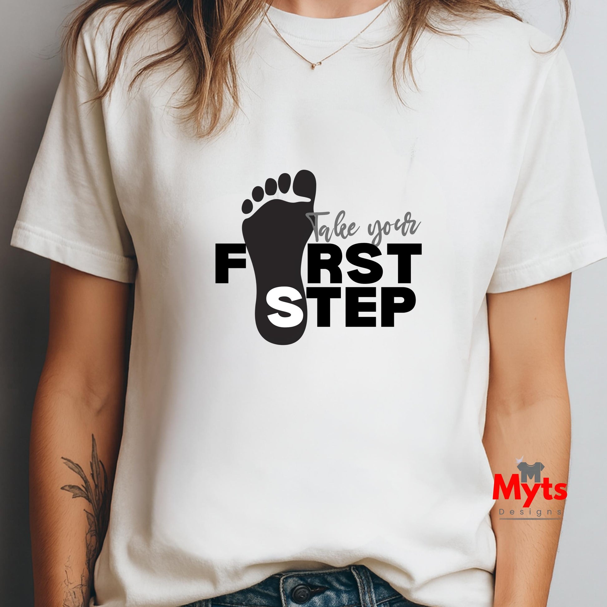 Person wearing a white t-shirt with a black footprint design and text 'Take your FIRST STEP' on a plain background.