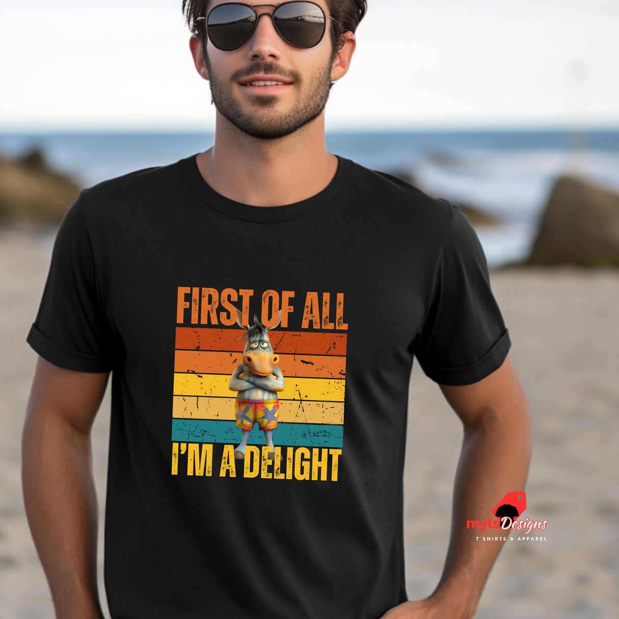 A man at the beach wearing a black "first of all I'm a delight" funny donkey t-shirt