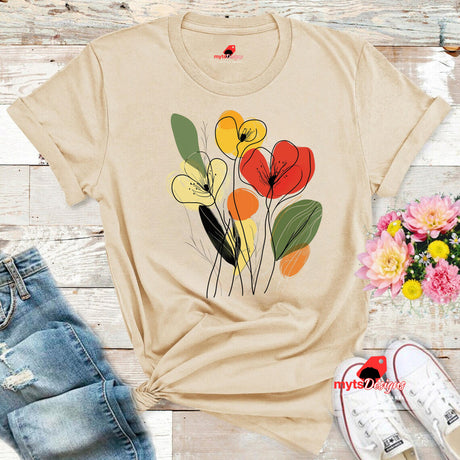Neutral t-shirt featuring minimalist floral line art with abstract red, yellow, and orange flowers and green leaves, laid flat on a wooden surface with rolled sleeves.