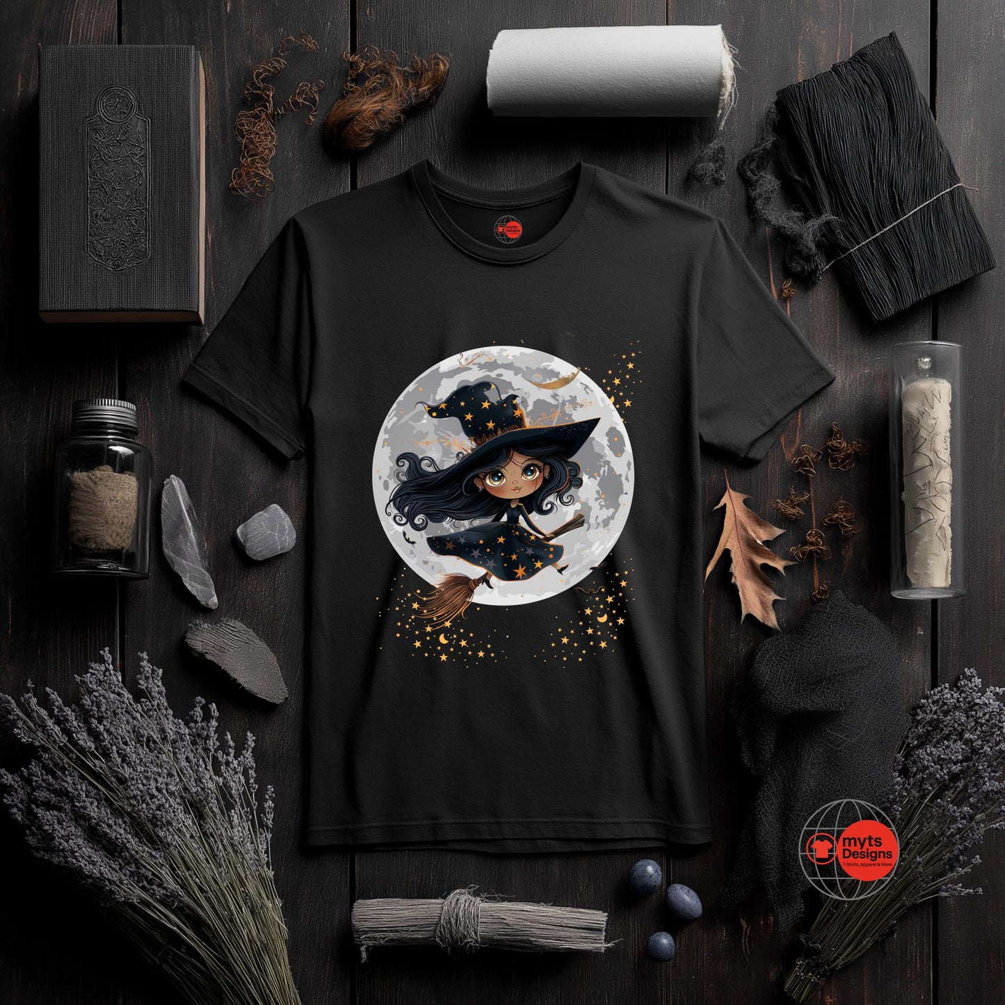 Black t-shirt with a witch graphic on a dark wooden surface with Halloween-themed decor.
