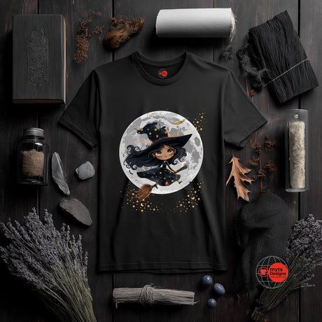 Black t-shirt with a witch graphic on a dark wooden surface with Halloween-themed decor.