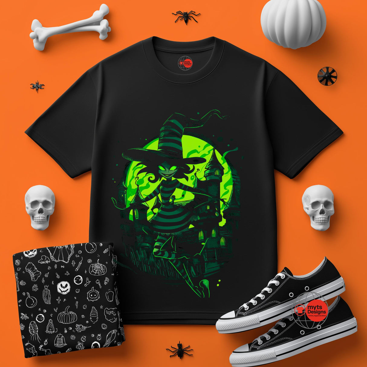 Black t-shirt with green witch design on an orange background with Halloween-themed accessories.