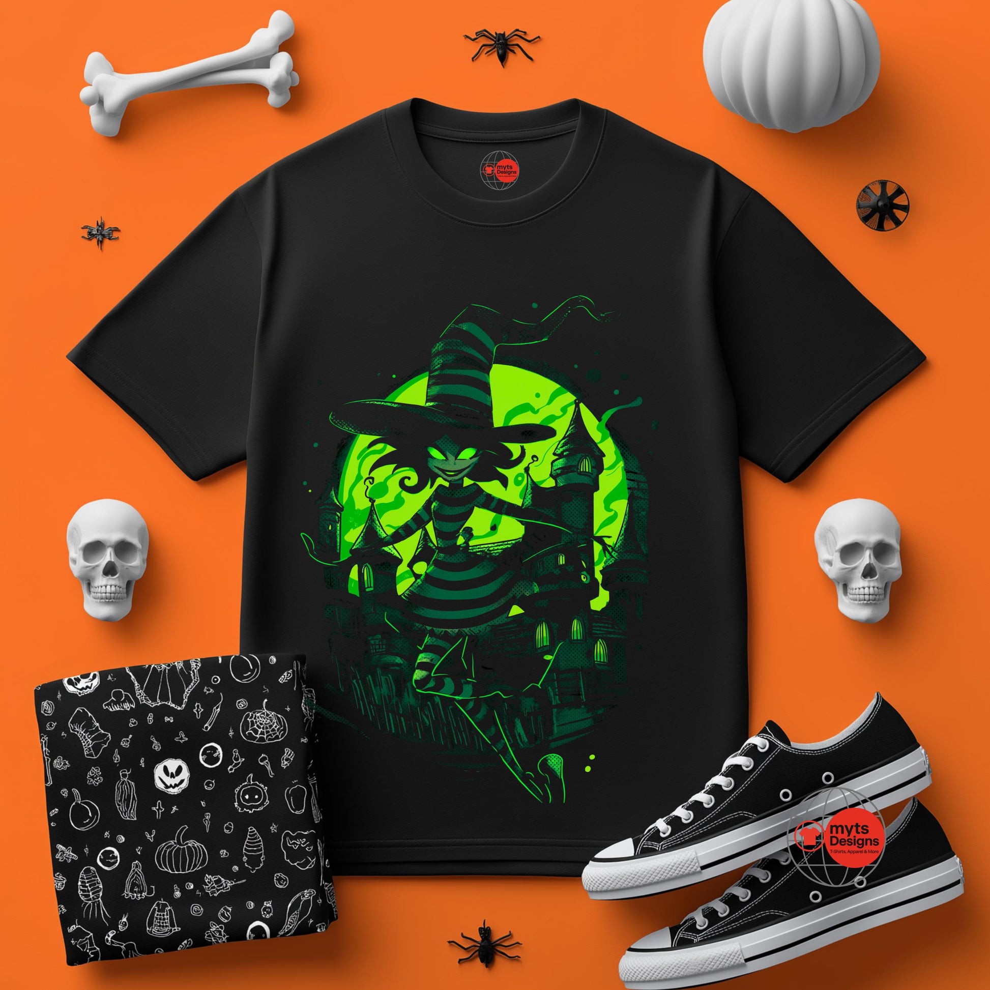 Black t-shirt with green witch design on an orange background with Halloween-themed accessories.