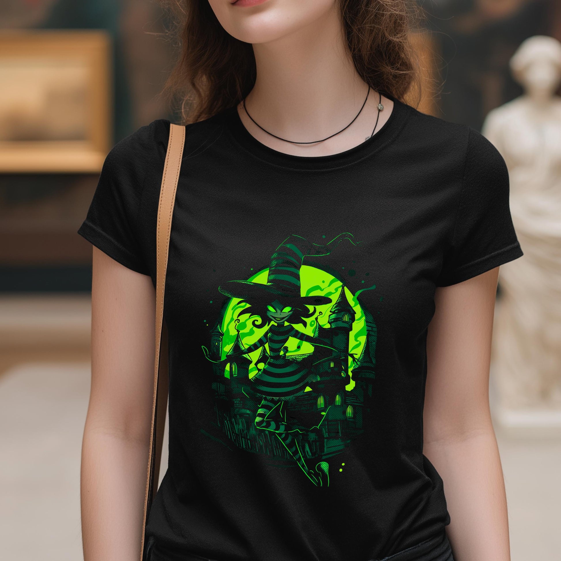 Person wearing a black t-shirt with a green graphic design of a witch and pumpkin.
