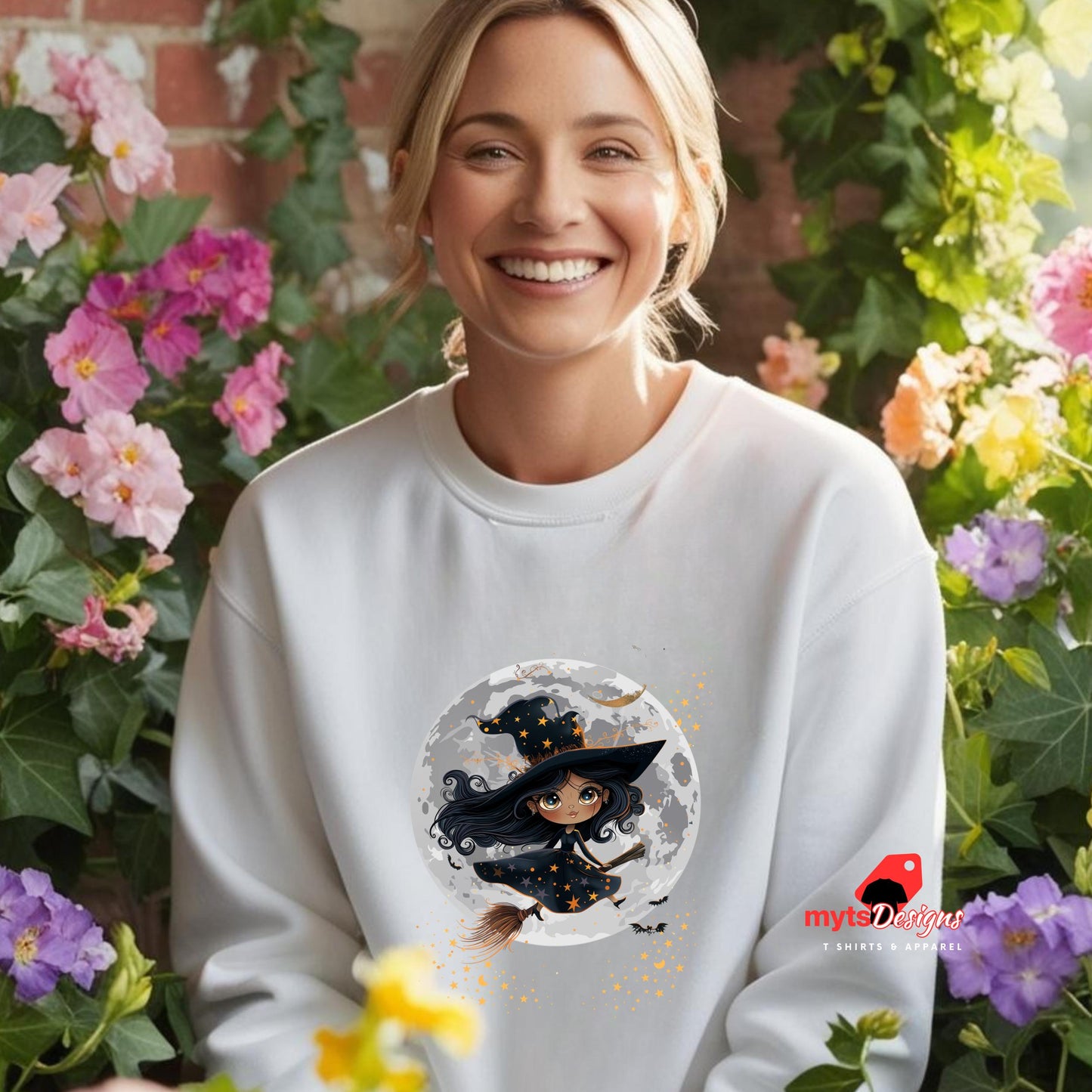 Woman wearing a white sweatshirt with a witch design, surrounded by flowers.