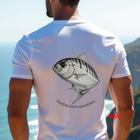 Man wearing a white t-shirt with a fish design on the back, standing by the ocean.