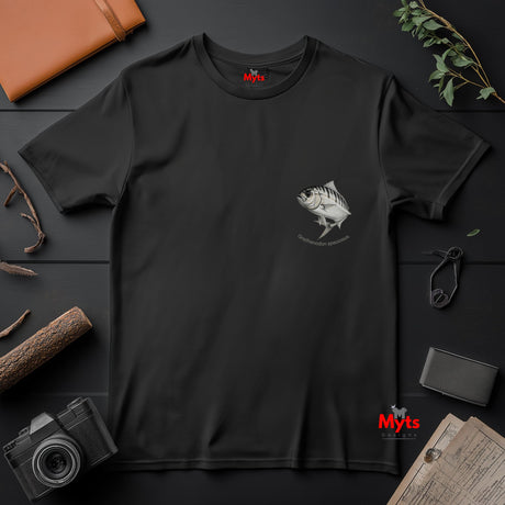 Black t-shirt with a fish graphic on a dark surface with a camera and wallet.