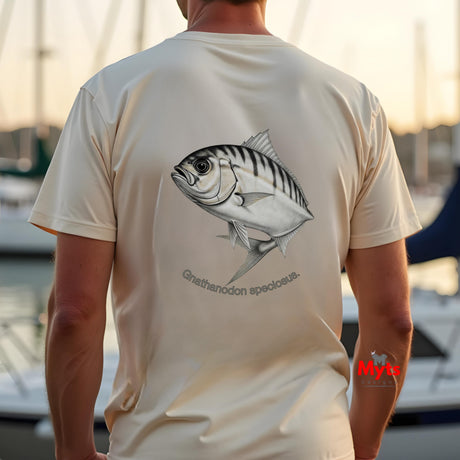 Person wearing a natural t-shirt with a fish design on the back, standing by water.