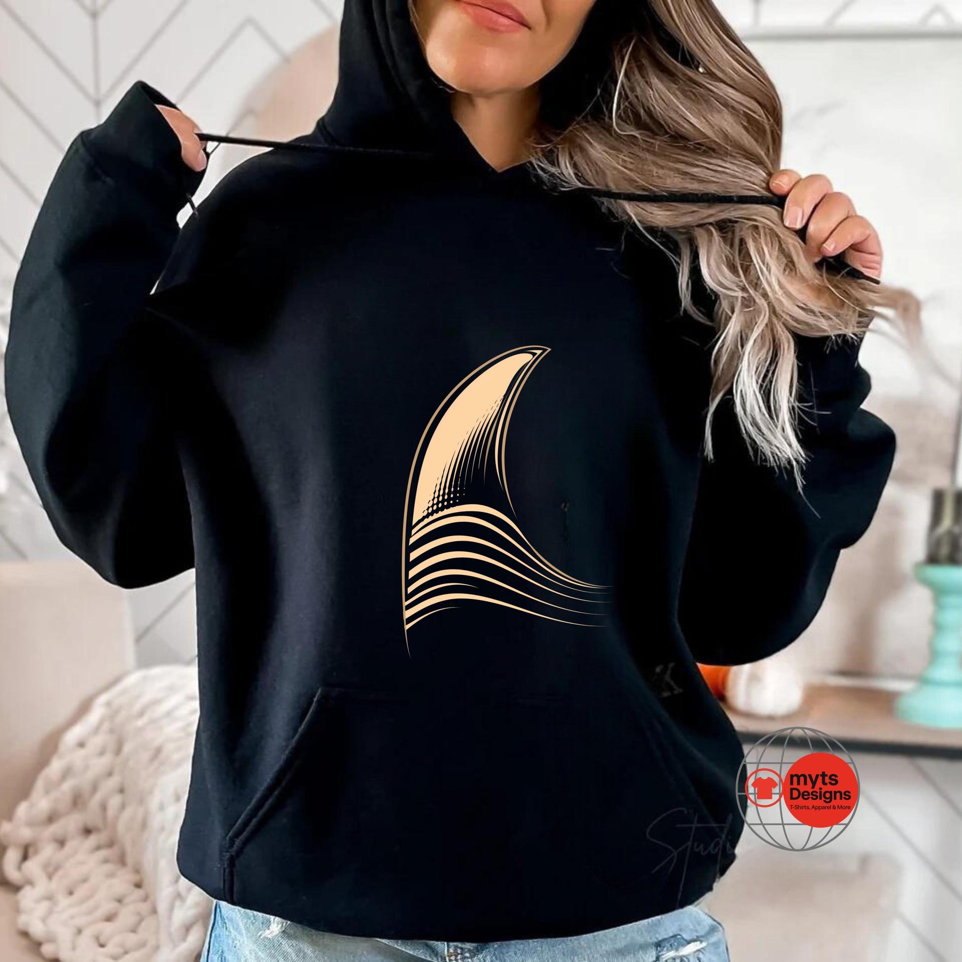 Person wearing a black hoodie with a gold design, sitting in a room.