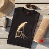 Black t-shirt with a gold graphic on a wooden surface with a hat, sunglasses, and towel.