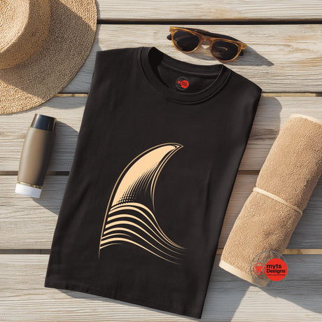 Black t-shirt with a gold graphic on a wooden surface with a hat, sunglasses, and towel.