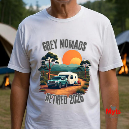 A man wearing a white graphic t-shirt with a retro-style camping scene print that reads 'GREY NOMADS RETIRED 2026'. The background is a blurred outdoor campsite with tents and fire pits.