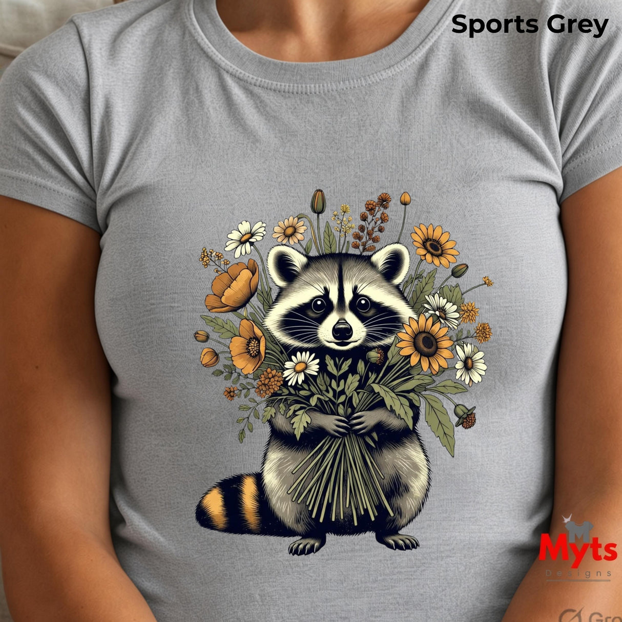 A light grey short-sleeve t-shirt featuring a detailed graphic of a raccoon holding a bouquet of wildflowers, worn by a model. The text 'Sports Grey' is visible in the top right corner, and a 'Myts' brand logo is in the bottom right.