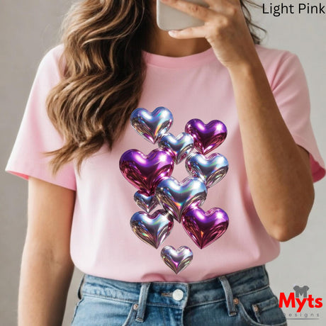 Person wearing a light pink t-shirt with metallic heart designs, holding a phone.