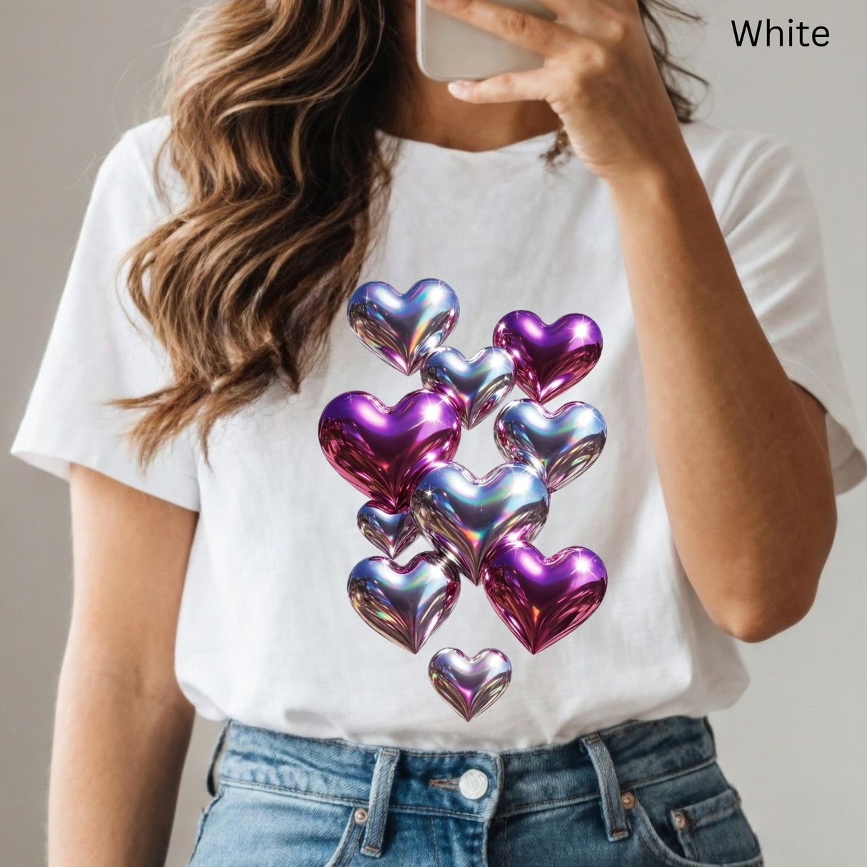 White t-shirt with colorful heart design worn by a person, holding a phone.