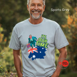 A man wearing a grey sports t-shirt with a graphic design and text, standing outdoors.