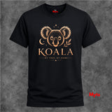 A black short-sleeve t-shirt with a gold graphic of a koala bear, a crescent moon, and the text 'KOALA MY TREE, MY HOME' on the front, displayed against a textured gray background.