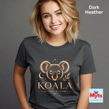 A woman wearing a dark heather gray t-shirt with a gold koala graphic and the text 'KOALA MY TREE, MY HOME'. The image has a 'Dark Heather' color label in the top right and a 'Myts Designs' logo in the bottom right corner.