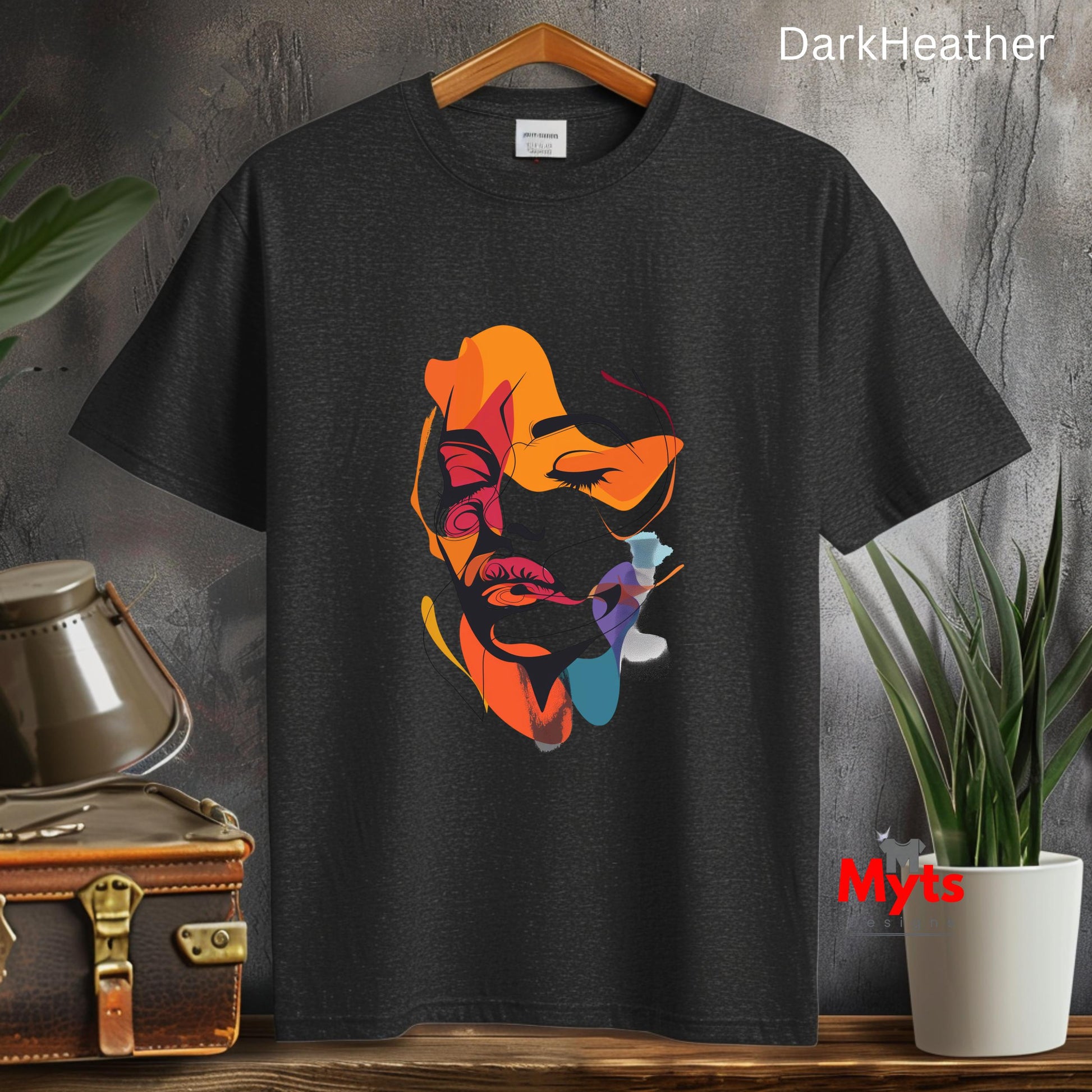 Black t-shirt with colorful graphic design on a wooden surface with plants and a suitcase.