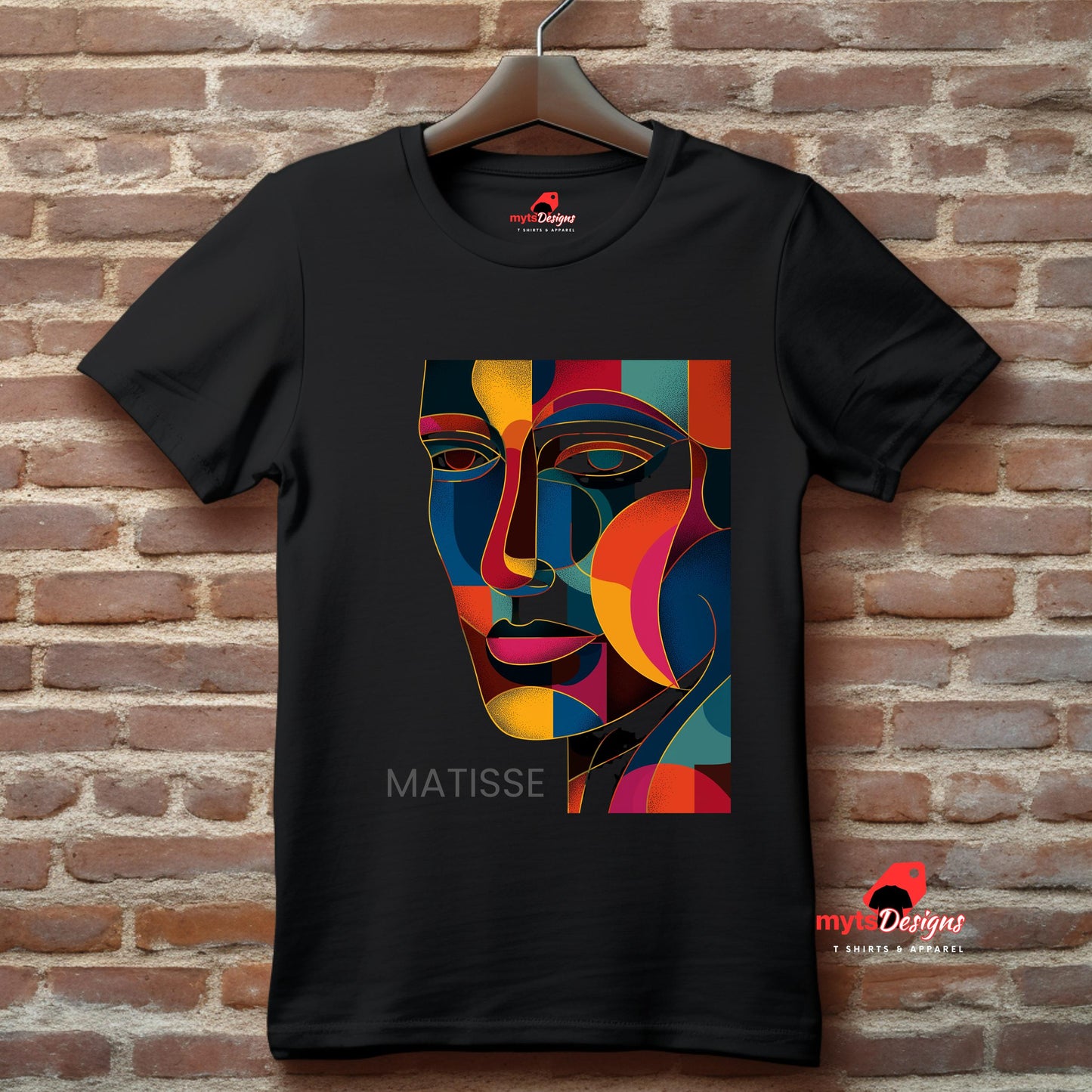 Black t-shirt featuring a vibrant geometric face design inspired by Henri Matisse, with rich colour blocks in red, blue, yellow, and orange. Shirt is displayed on hanger against a brick wall, emphasizing the bold contrast and modernist aesthetic. MytsDesigns logo is visible.