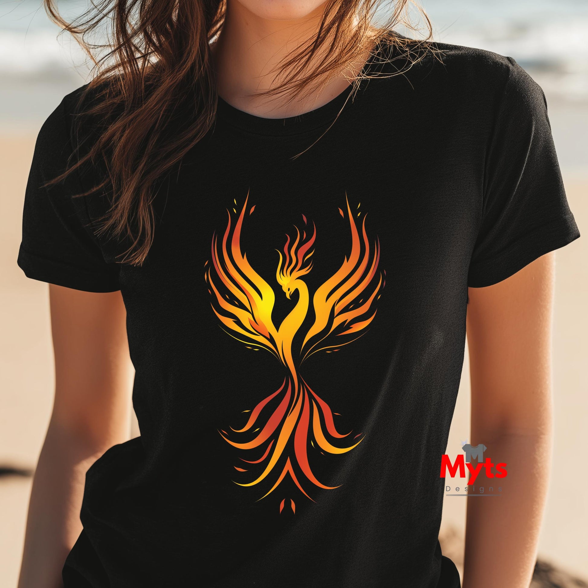 Person wearing a black t-shirt with a colorful phoenix design on a beach.