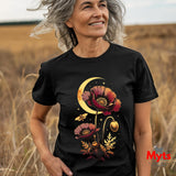 A smiling older woman standing in a field of dry grass wearing a black graphic T-shirt. The shirt features a detailed print of red poppy flowers, a crescent moon, stars, and small butterflies in warm gold, orange, and red tones.