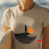 Person wearing a sand t-shirt with a wave and sun design, standing on sand with ocean view.