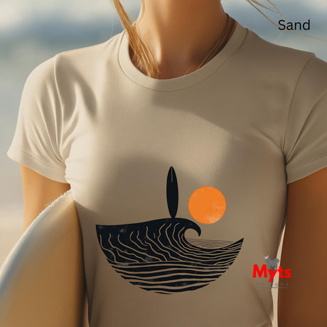 Person wearing a sand t-shirt with a wave and sun design, standing on sand with ocean view.