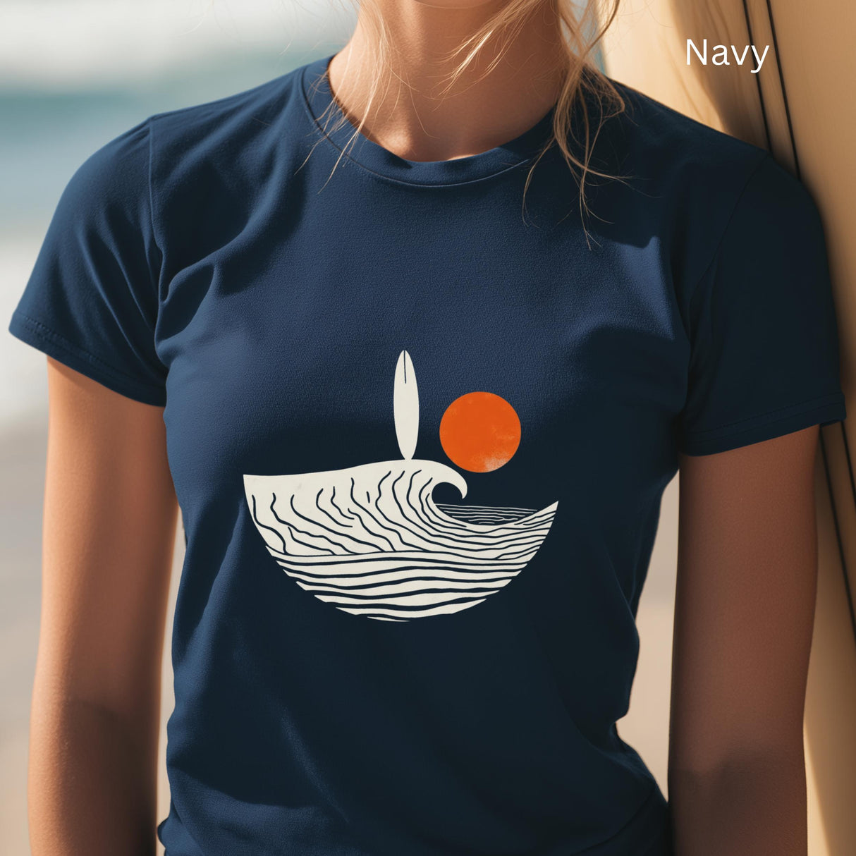 Navy t-shirt with a wave and sun design worn by a person on a beach.