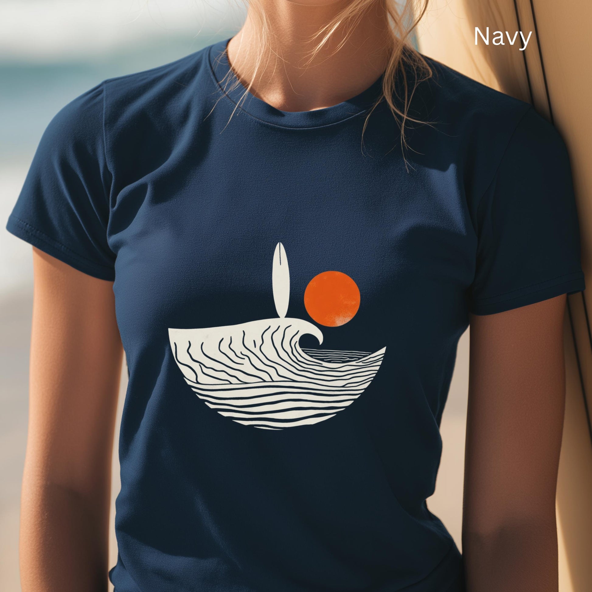Navy t-shirt with a wave and sun design worn by a person on a beach.