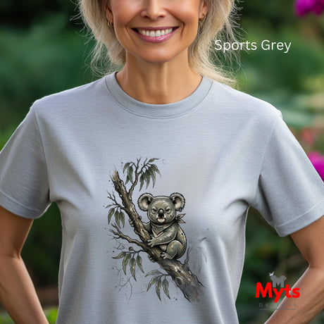 A woman wearing a light grey short-sleeve t-shirt with a detailed black and white koala graphic on the front, set against a blurred green garden background. The text 'Sports Grey' is visible in the top right, and a 'Myts Designs' logo is in the bottom right.