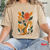 A woman wearing a Sand graphic t-shirt with a kangaroo and floral design, paired with ripped blue jeans, sitting on a white couch. The text 'Sand' is visible in the top right corner.