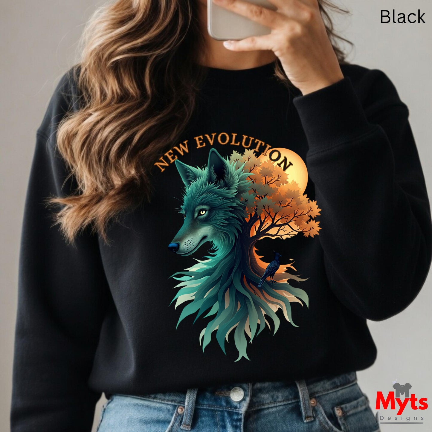 A woman wearing a black crewneck sweatshirt with a detailed graphic of a teal wolf and an orange autumn tree under a yellow sun, with the text 'NEW EVOLUTION' above. She is taking a mirror selfie, and the image has a 'Myts Designs' watermark in the bottom right corner.