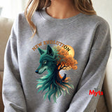 A person wearing a heather gray crewneck sweatshirt with a large graphic print on the front. The graphic features a teal wolf head merging with an orange autumn tree and a glowing orange moon, with the words 'NEW EVOLUTION' arched above.