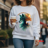 A woman wearing a white crewneck sweatshirt with a colorful graphic of a wolf and tree, holding a coffee cup in an outdoor urban setting.