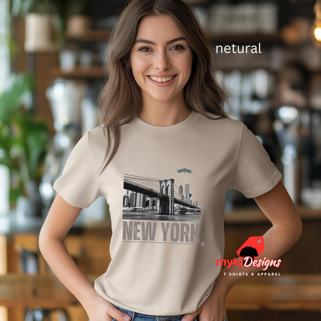 Netural colored soft casual tee showing the New York City skyline with a stylized spaceship graphic soaring above, Worn by a young woman.